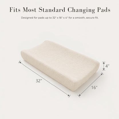 Changing pad cover in cream/off-white textured muslin fabric shown on a contoured pad. Dimension arrows indicate 32" long x 16" wide x 4" tall. Text reads 'Fits Most Standard Changing Pads.'