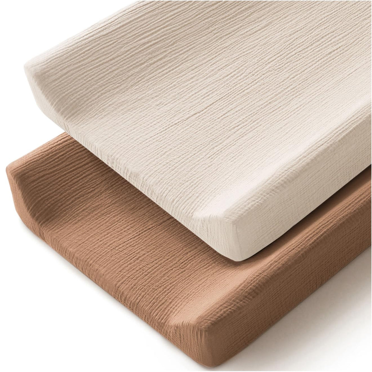 Two changing pad covers stacked at an angle on a white background. The top cover is cream/off-white and the bottom is warm tan/caramel. Both feature a crinkled muslin texture and wrap snugly around rectangular foam pads.
