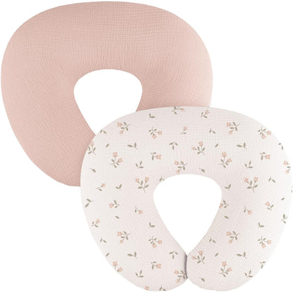Two U-shaped nursing pillow covers in a textured muslin fabric. The back cover is solid dusty pink; the front cover is cream/white with a small scattered floral pattern in pink blooms and sage green leaves.