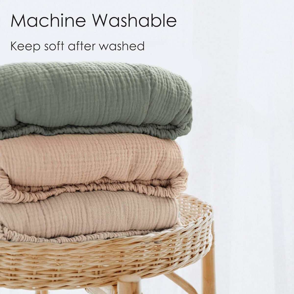 Three folded muslin fitted crib sheets stacked on a wicker stool: sage green on top, blush pink in the middle, and taupe on the bottom. Text reads 'Machine Washable - Keep soft after washed.'