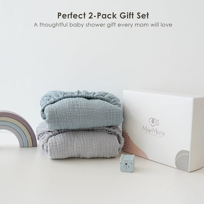 Two folded muslin fitted bassinet sheets stacked together -- one light blue on top, one gray below -- displayed beside a white MairMore gift box. Text reads 'Perfect 2-Pack Gift Set, A thoughtful baby shower gift every mom will love.'