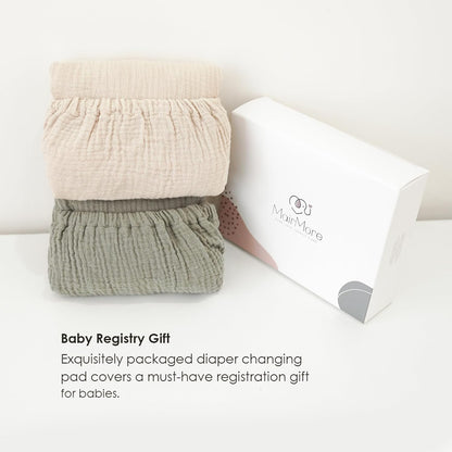 Two folded muslin changing pad covers stacked together -- one light beige and one sage green -- beside a white MairMore gift box. Text reads 'Baby Registry Gift: Exquisitely packaged diaper changing pad covers a must-have registration gift for babies.'