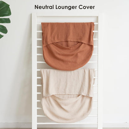 Two muslin lounger covers draped over a white ladder rack. The top cover is terracotta/caramel orange and the bottom is cream/off-white. Both show a curved pouch shape with textured cotton weave. Text reads 'Neutral Lounger Cover.'