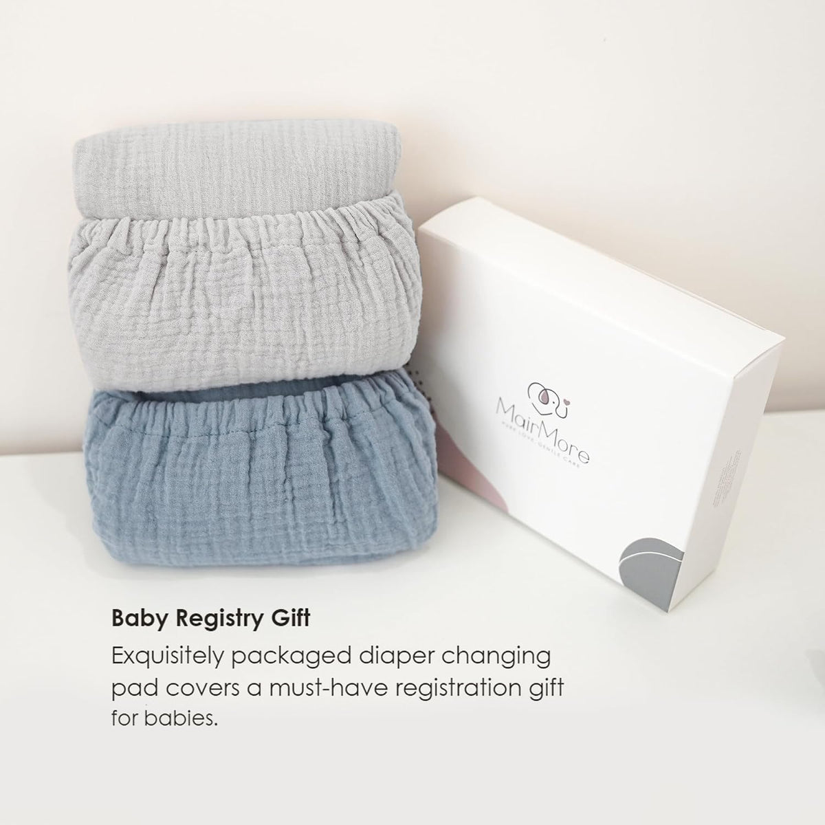 Two folded muslin changing pad covers stacked together -- one light gray on top, one dusty blue on bottom -- beside a white MairMore gift box. Text reads 'Baby Registry Gift' with a brief product description.