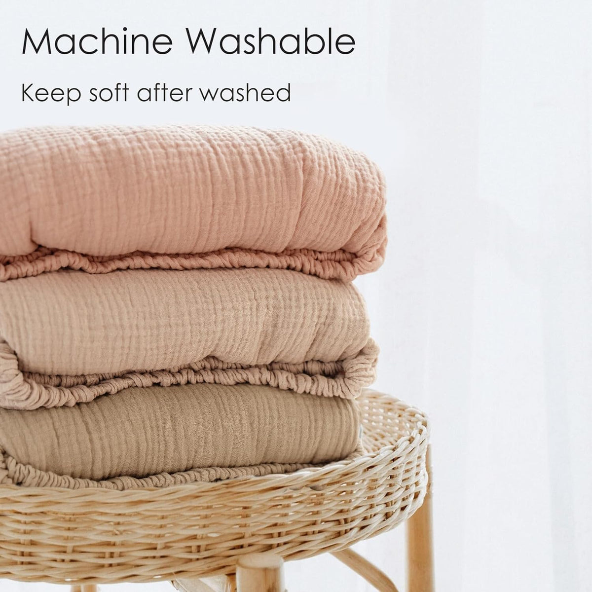 Three folded muslin cotton blankets stacked on a wicker stool, in dusty rose, light tan, and khaki. Crinkled texture visible. Text reads 'Machine Washable - Keep soft after washed.'