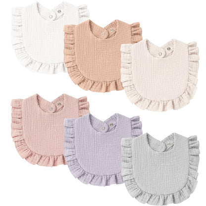 Six ruffled baby bibs in muslin cotton arranged in two rows: white, tan, and cream on top; dusty pink, lavender, and light gray on bottom. Each bib has snap closures at the neck and a ruffled hem edge.