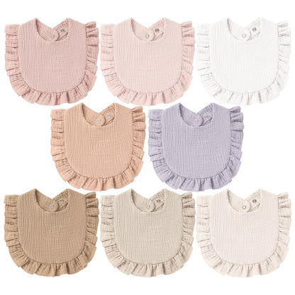 Eight ruffled baby bibs in a variety of soft colors: dusty rose, light pink, white, peach, lavender, tan, beige, and cream. Each bib has a crinkled muslin texture, ruffle trim along the bottom edge, and snap closures at the neck.