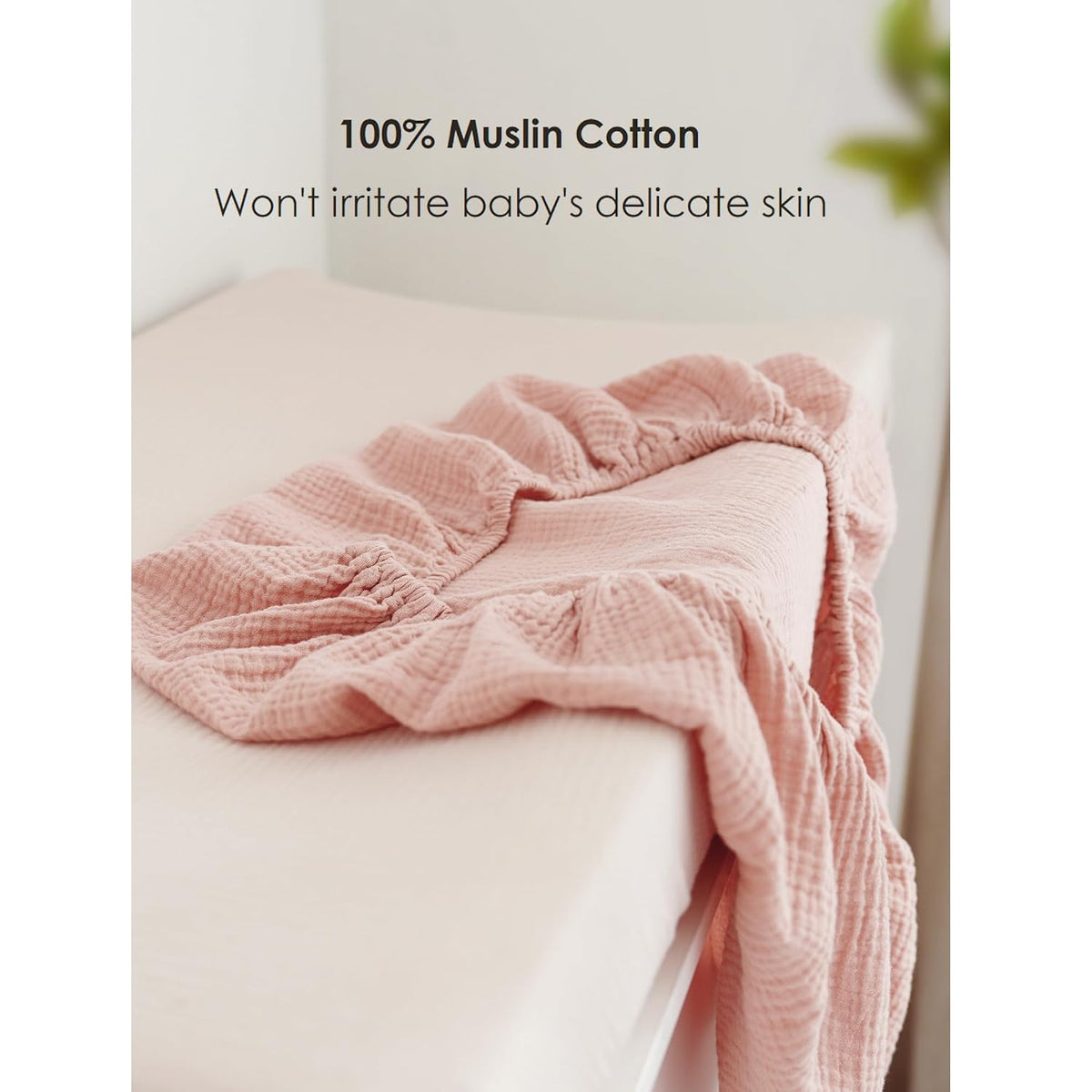 A dusty pink muslin cotton changing pad cover with visible crinkled texture and elasticized edges, loosely folded atop a cream-colored changing pad. Text reads '100% Muslin Cotton - Won't irritate baby's delicate skin.'