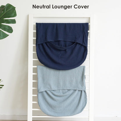 Two muslin baby lounger covers draped over a white ladder rack. The top cover is dark navy blue and the bottom is light dusty blue, both showing a textured woven fabric with a curved pouch shape. Text reads 'Neutral Lounger Cover'.