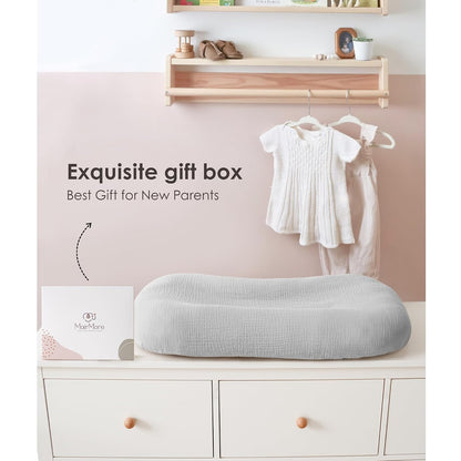 Light gray textured muslin baby lounger cover draped over a curved infant lounger, displayed on a white dresser beside a gift box. Text reads 'Exquisite gift box - Best Gift for New Parents.' Nursery setting with baby clothes hanging nearby.