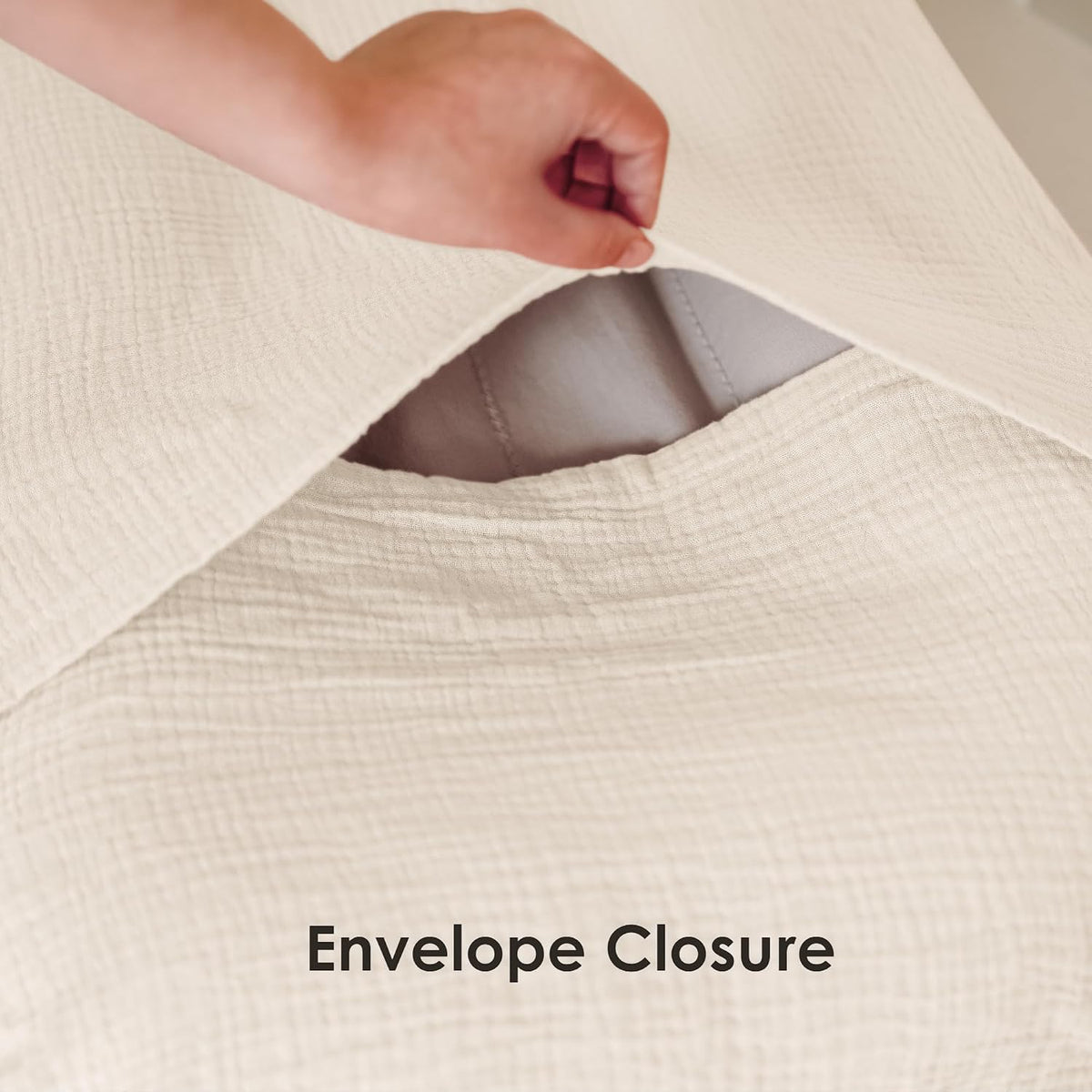 Close-up of a cream-colored textured muslin pillow cover being lifted to reveal an envelope closure, showing a gray quilted insert inside. Bold text at bottom reads 'Envelope Closure'.