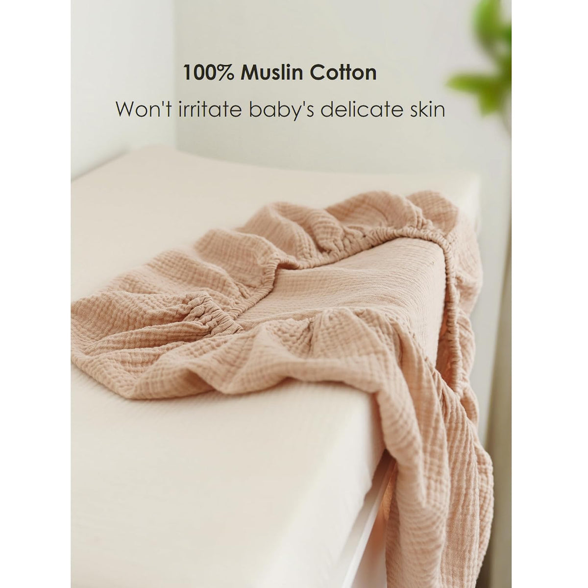 A dusty rose/clay-colored muslin cotton changing pad cover with visible crinkled texture and elasticized edges, draped over a white changing pad. Text reads '100% Muslin Cotton - Won't irritate baby's delicate skin.'