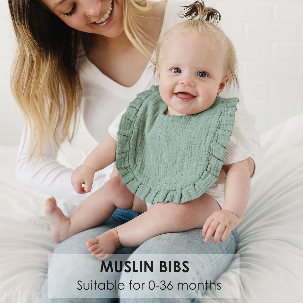 Smiling baby wearing a sage green muslin bib with ruffled edges, seated on an adult's lap. Text reads 'MUSLIN BIBS - Suitable for 0-36 months.' Bib has a soft, textured cotton appearance.