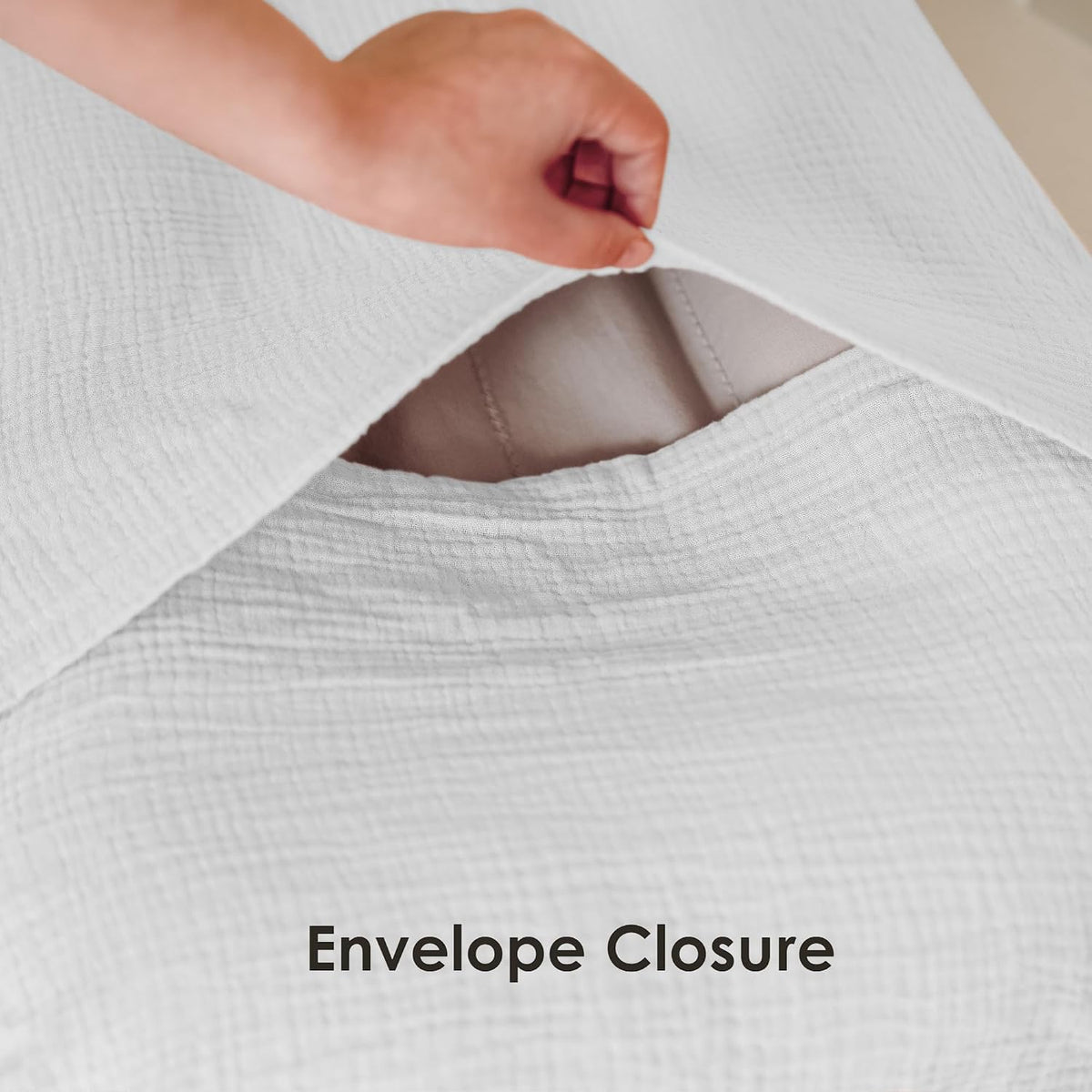 Close-up of a white textured muslin fabric cover being lifted to reveal an envelope closure opening, showing a gray interior lining beneath. Text below reads 'Envelope Closure'.