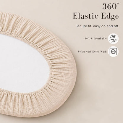 Oval fitted bassinet sheet in light beige muslin fabric shown fitted over a mattress, with gathered elastic edging visible around the full perimeter. Text reads '360 Elastic Edge - Secure fit, easy on and off. Soft & Breathable. Softer with Every Wash.'