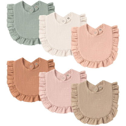 Six ruffled baby bibs in a flat lay arrangement, shown in sage green, cream, peach, rust, light pink, and tan. Each bib features a crinkled muslin texture, ruffle trim along the bottom edge, and snap closures at the shoulder.