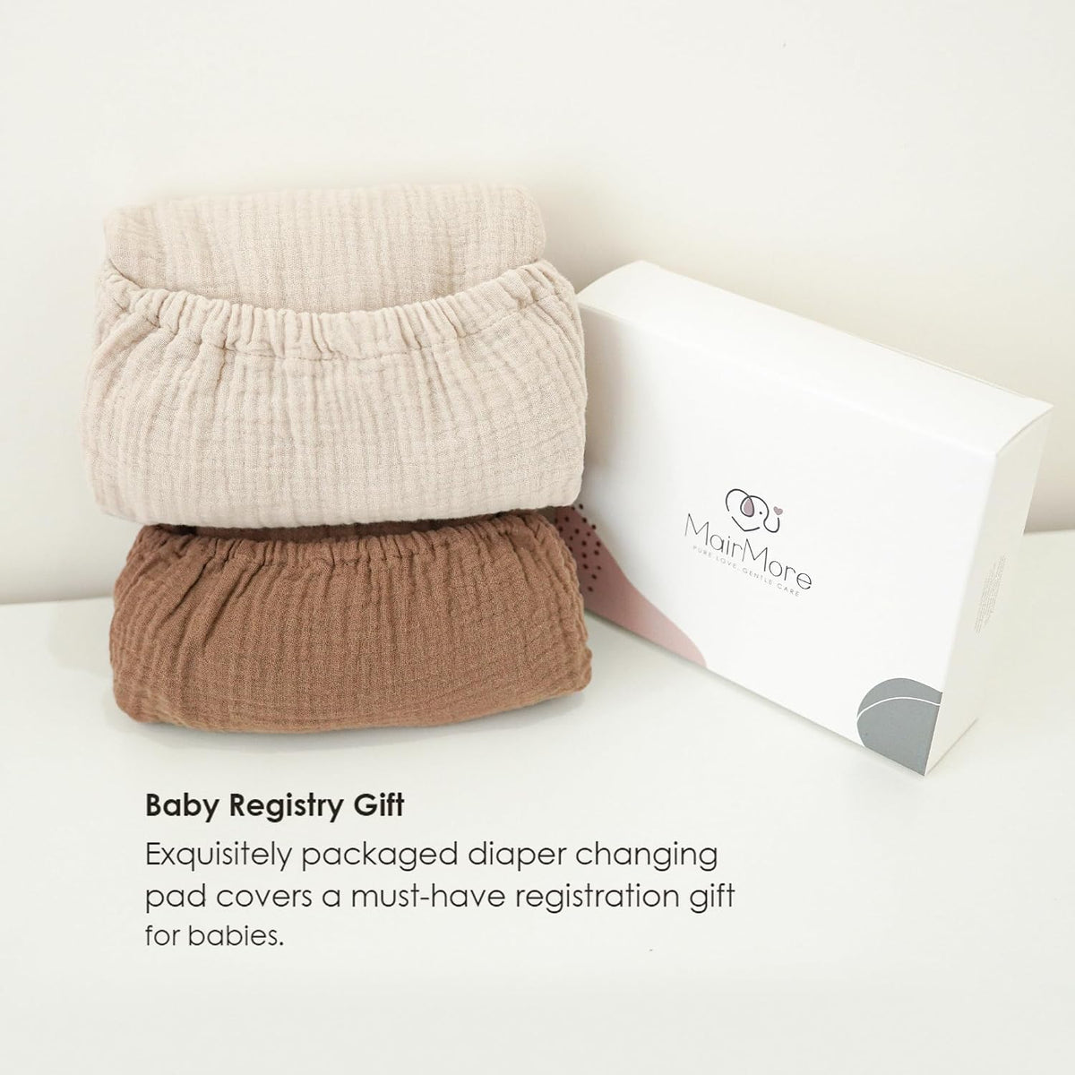 Two folded muslin changing pad covers stacked together -- one light beige and one medium brown -- beside a white MairMore gift box. Text reads 'Baby Registry Gift' with a brief product description below.