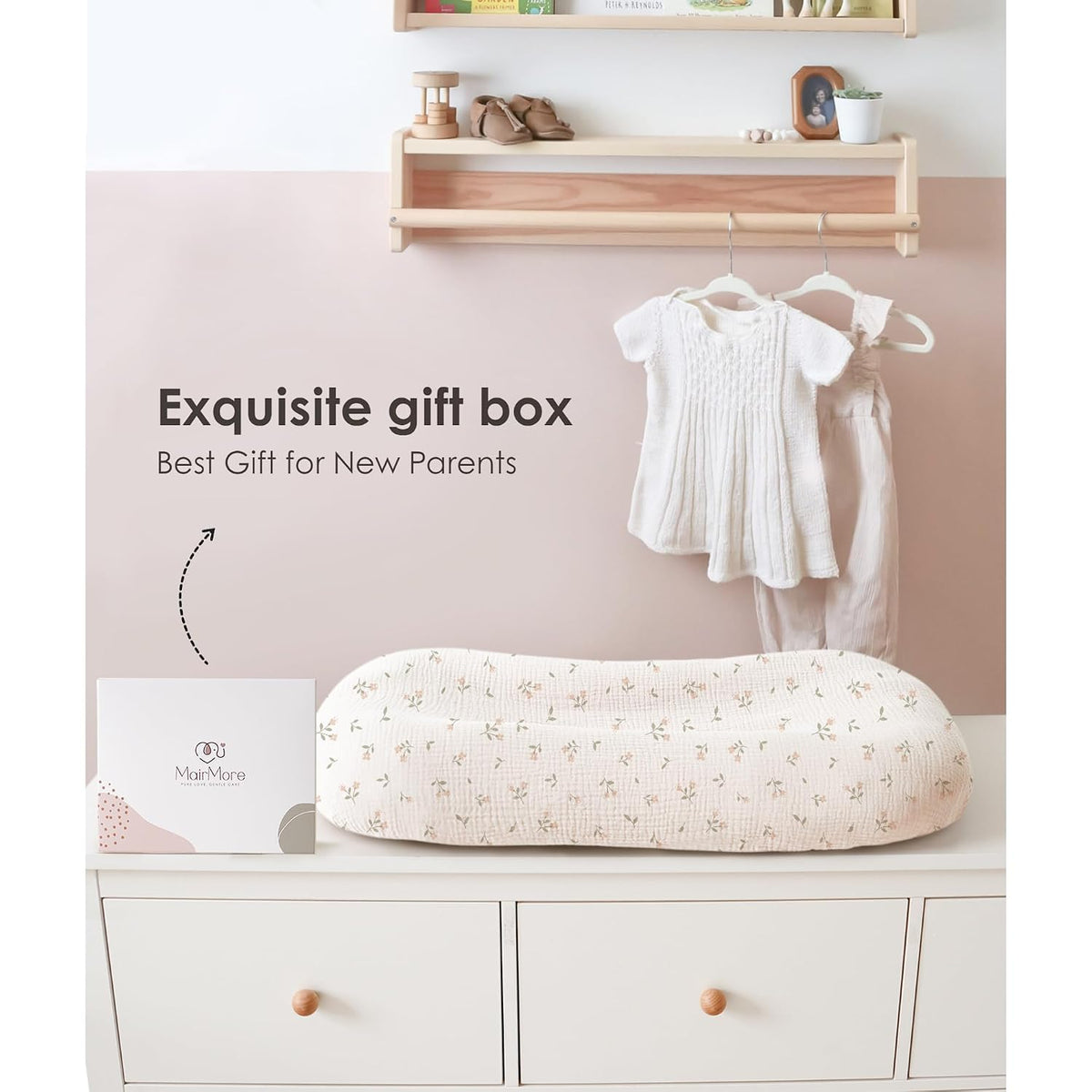 Baby lounger cover in cream muslin fabric with a delicate pink floral blossom pattern, displayed on a white dresser beside a MairMore gift box. Text reads 'Exquisite gift box - Best Gift for New Parents.'