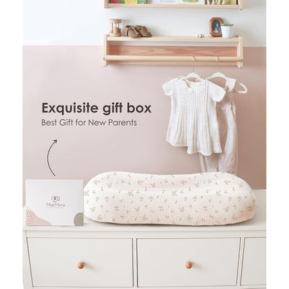 Baby lounger cover in cream muslin fabric with a delicate pink floral blossom pattern, displayed on a white dresser beside a MairMore gift box. Text reads 'Exquisite gift box - Best Gift for New Parents.'