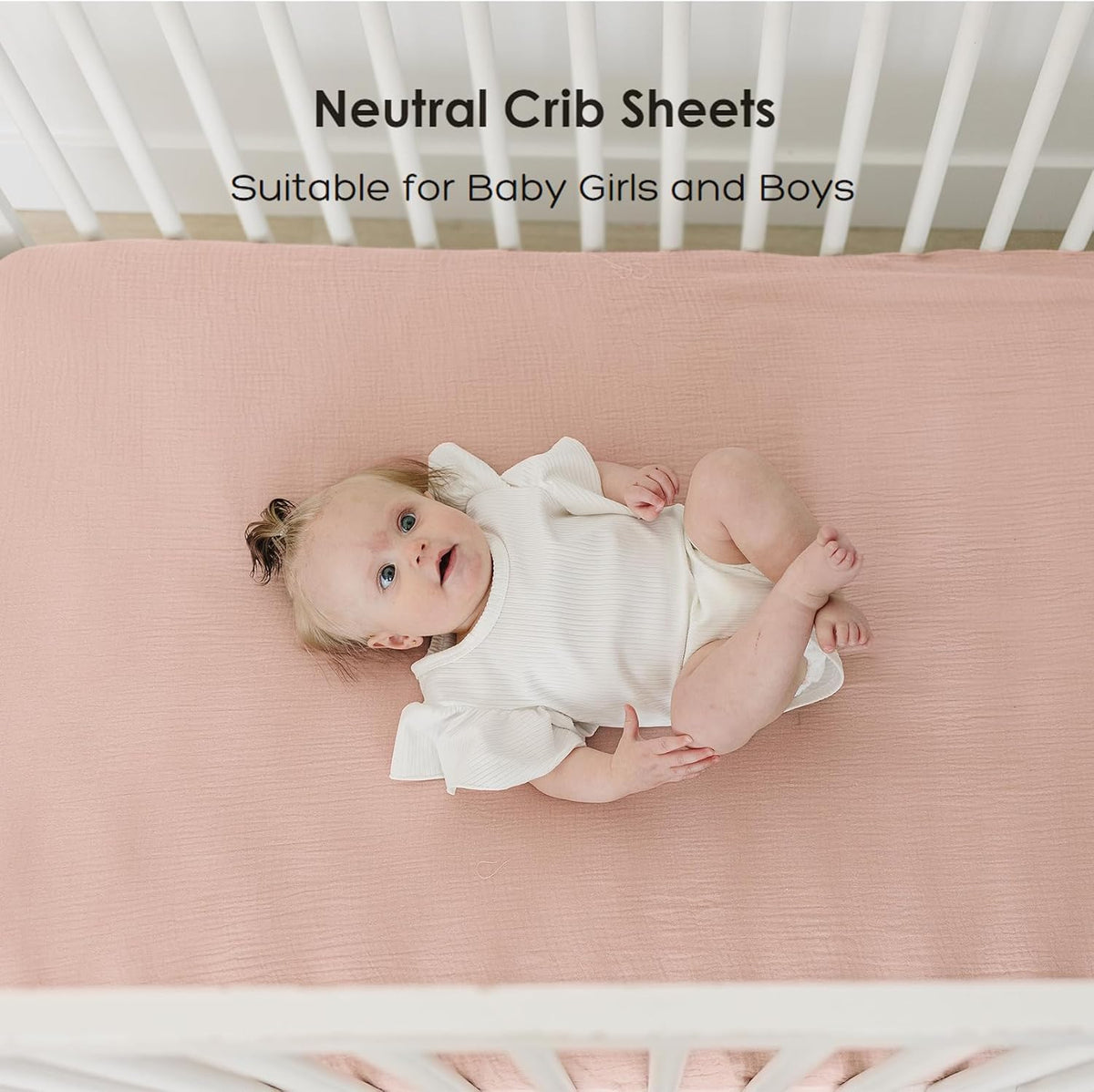 Overhead view of a baby lying on a dusty rose fitted crib sheet with a subtle textured weave, inside a white crib. Text reads 'Neutral Crib Sheets - Suitable for Baby Girls and Boys.'