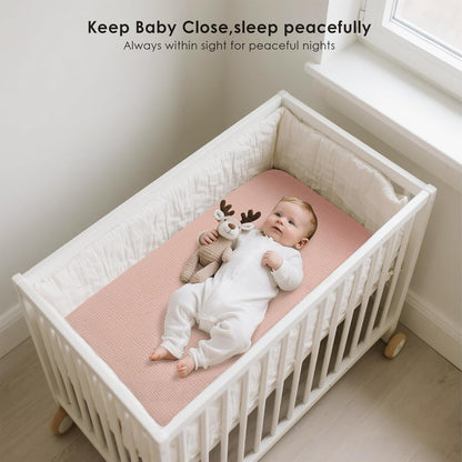 Baby lying in a white crib on a dusty pink fitted sheet, holding a knit reindeer toy. Text reads 'Keep Baby Close, sleep peacefully. Always within sight for peaceful nights.'