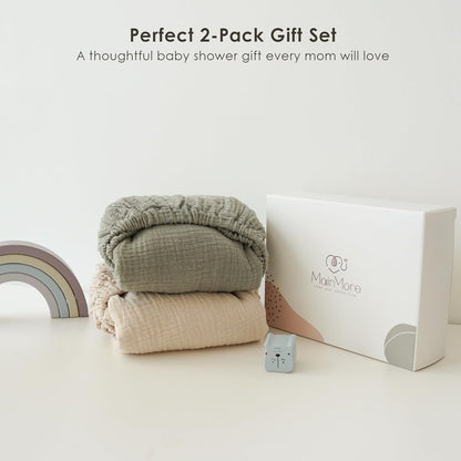 Two folded muslin fitted bassinet sheets stacked together -- sage green on top, light beige below -- displayed beside a white MainMore gift box. Text reads 'Perfect 2-Pack Gift Set, A thoughtful baby shower gift every mom will love.'