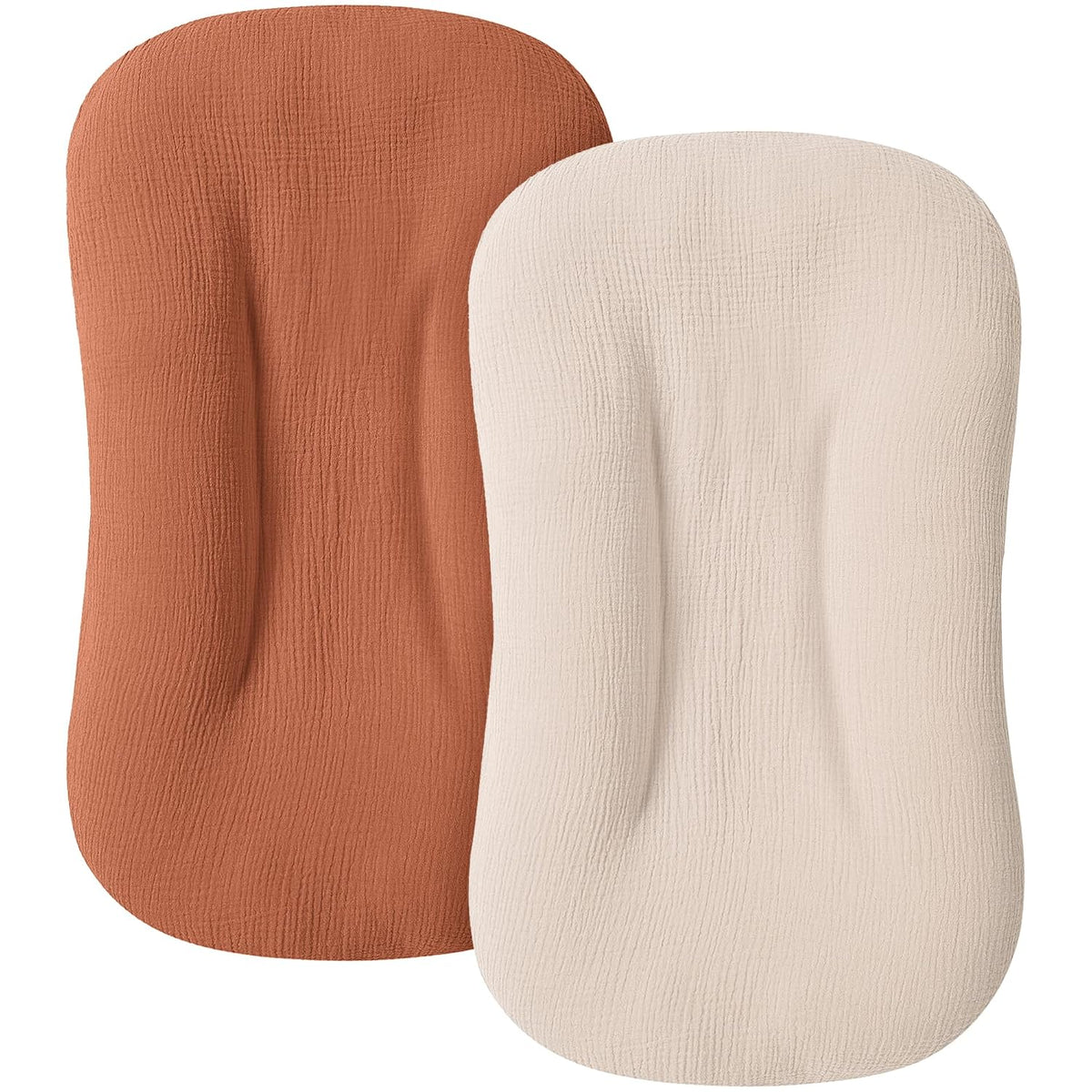 Two fitted baby lounger covers in a textured muslin fabric, shown overlapping. Left cover is terracotta/caramel orange; right cover is cream/off-white. Both have a rounded rectangular shape with contoured edges.