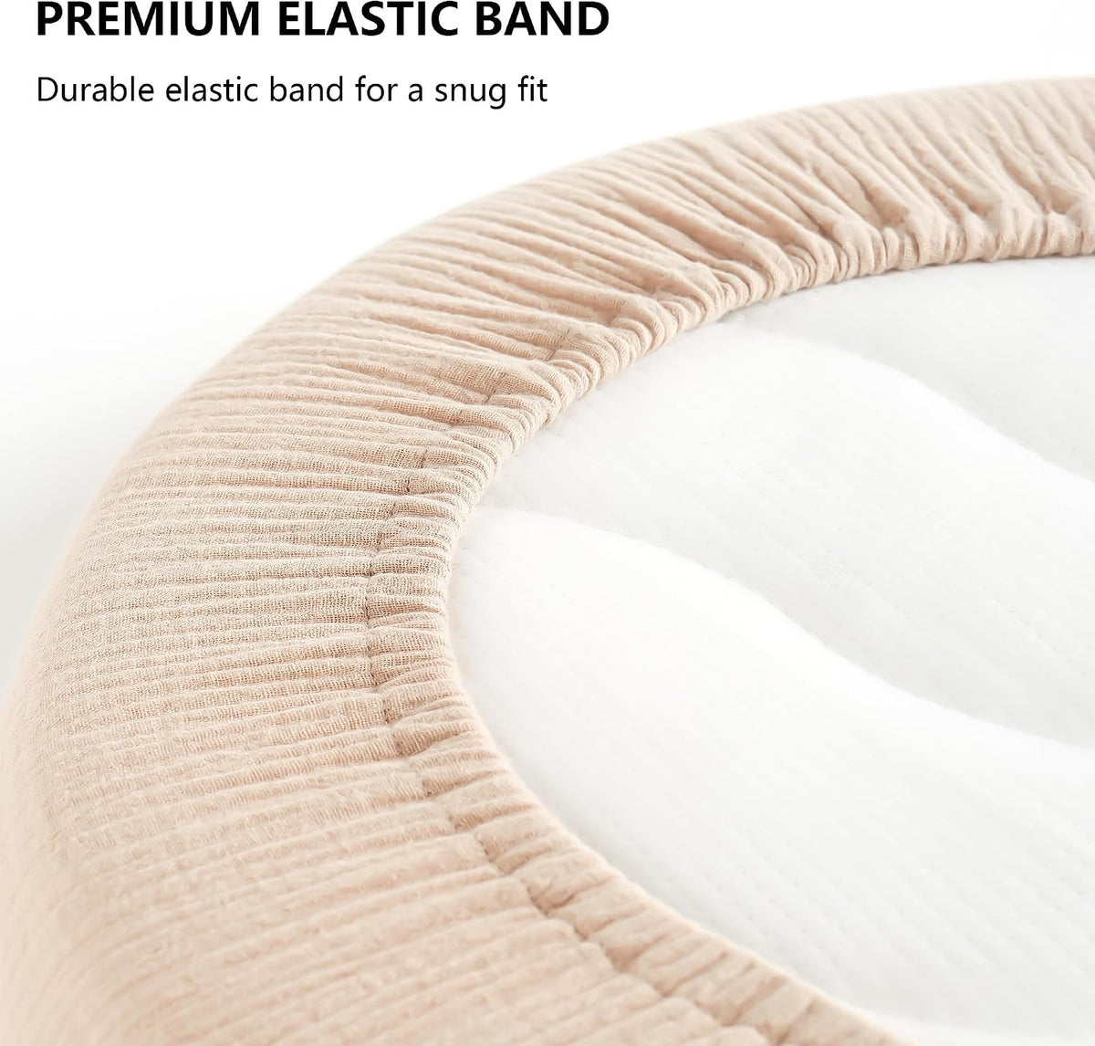Close-up of a beige ribbed fabric fitted sheet with a visible elastic band stretched around the curved edge of a white oval bassinet mattress. Text reads 'Premium Elastic Band - Durable elastic band for a snug fit.'