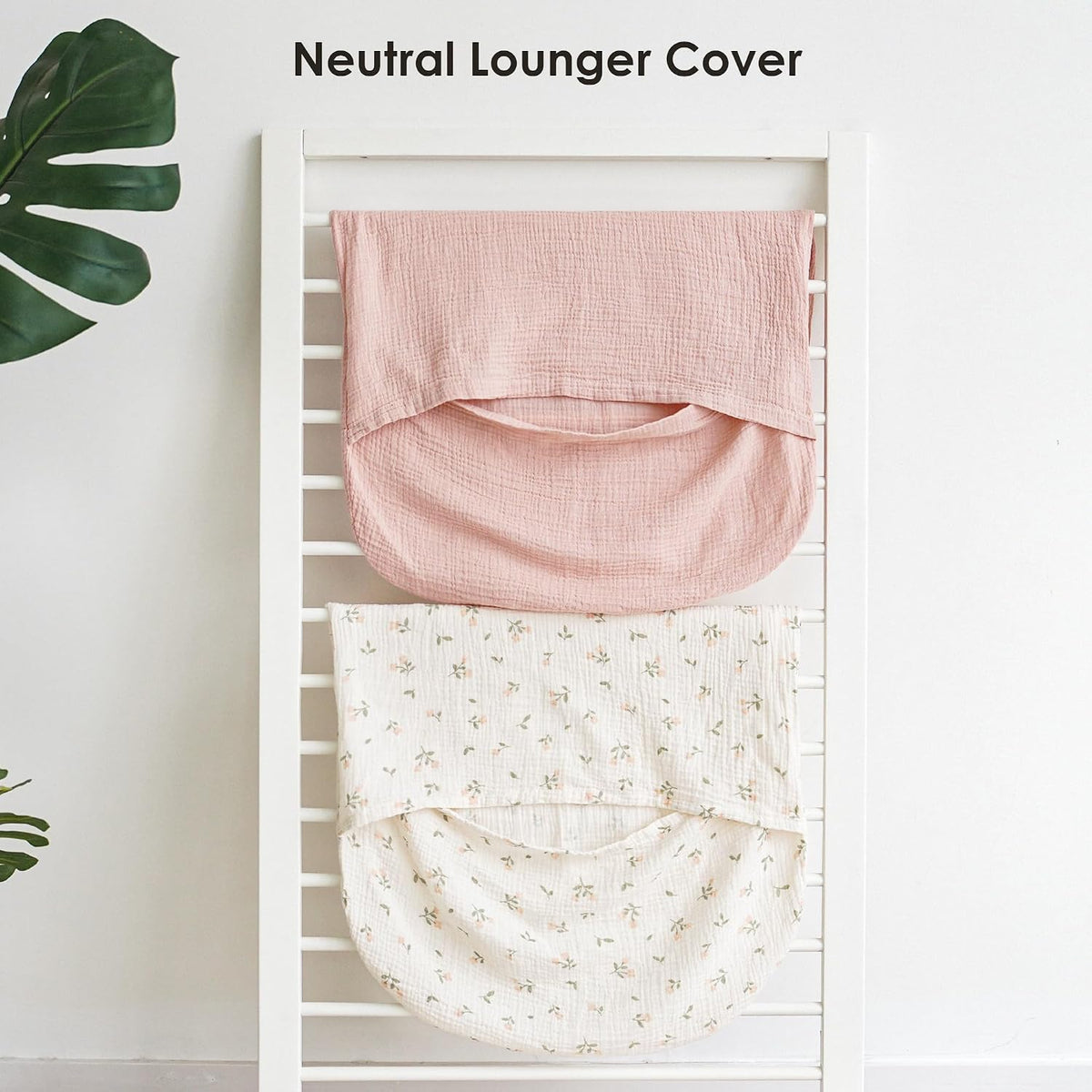 Two muslin baby lounger covers draped over a white rack. The top cover is solid dusty pink; the bottom is cream with a small floral print. Both show a curved pocket shape. Text reads 'Neutral Lounger Cover'.
