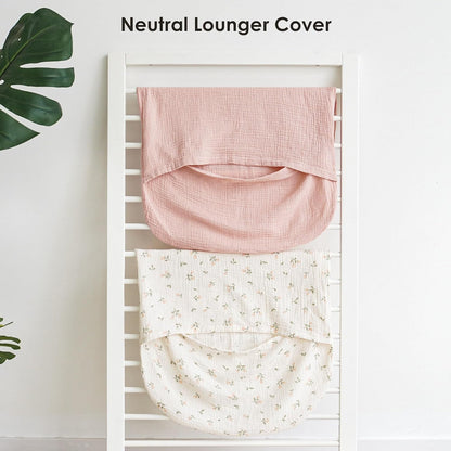 Two muslin baby lounger covers draped over a white rack. The top cover is solid dusty pink; the bottom is cream with a small floral print. Both show a curved pocket shape. Text reads 'Neutral Lounger Cover'.