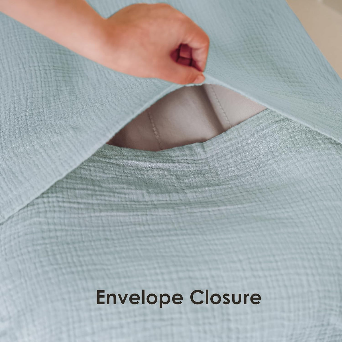 A hand lifts the flap of a light blue textured muslin fabric cover, revealing a white interior lining and the envelope-style opening. Text below reads 'Envelope Closure'.