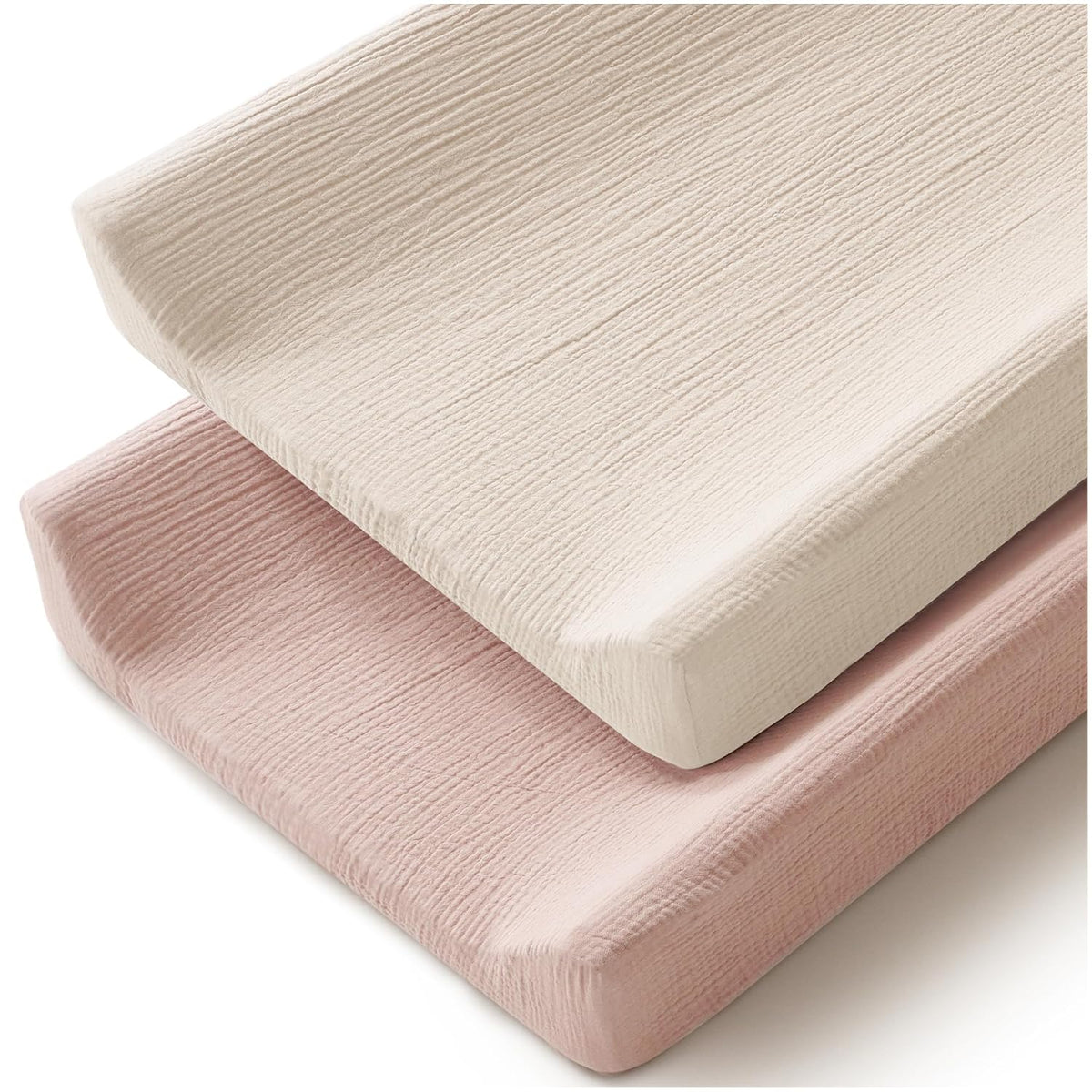 Two changing pad covers stacked at an angle on a white background. The top cover is ivory/cream and the bottom is soft blush pink. Both feature a crinkled muslin cotton texture with fitted edges.