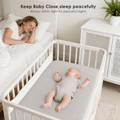 Lifestyle image of a white bedside bassinet with a baby sleeping on a light gray fitted sheet. A woman rests in the adjacent bed. Text reads 'Keep Baby Close, sleep peacefully. Always within sight for peaceful nights.'