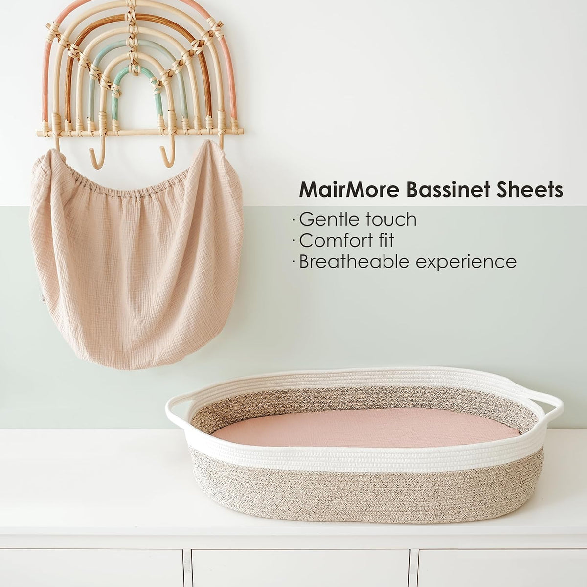 MairMore Bassinet Sheets shown two ways: a blush muslin fitted sheet hanging from a decorative rainbow wall hook, and a pink fitted sheet stretched over an oval rope bassinet on a white dresser. Text lists: Gentle touch, Comfort fit, Breathable experience.