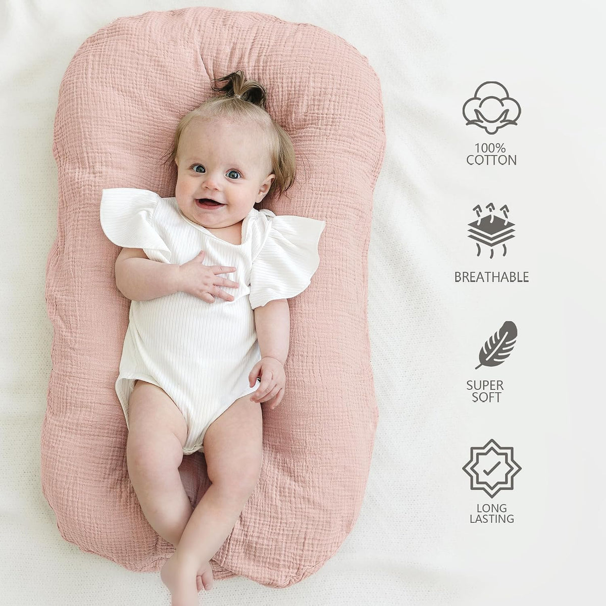Baby lying in a dusty pink muslin cotton lounger, smiling in a white ruffle onesie. Icons on the right highlight: 100% Cotton, Breathable, Super Soft, and Long Lasting.