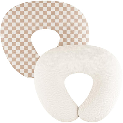Two U-shaped nursing pillow covers on a white background. The back cover features a tan and cream checkerboard pattern; the front cover is solid cream with a visible woven muslin texture. Both have a U-shaped opening.
