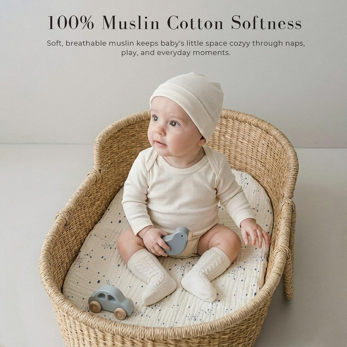 Baby seated in a wicker bassinet on a white muslin fitted sheet printed with small blue stars and star clusters. Text reads '100% Muslin Cotton Softness' with a tagline about breathable muslin for naps, play, and everyday moments.