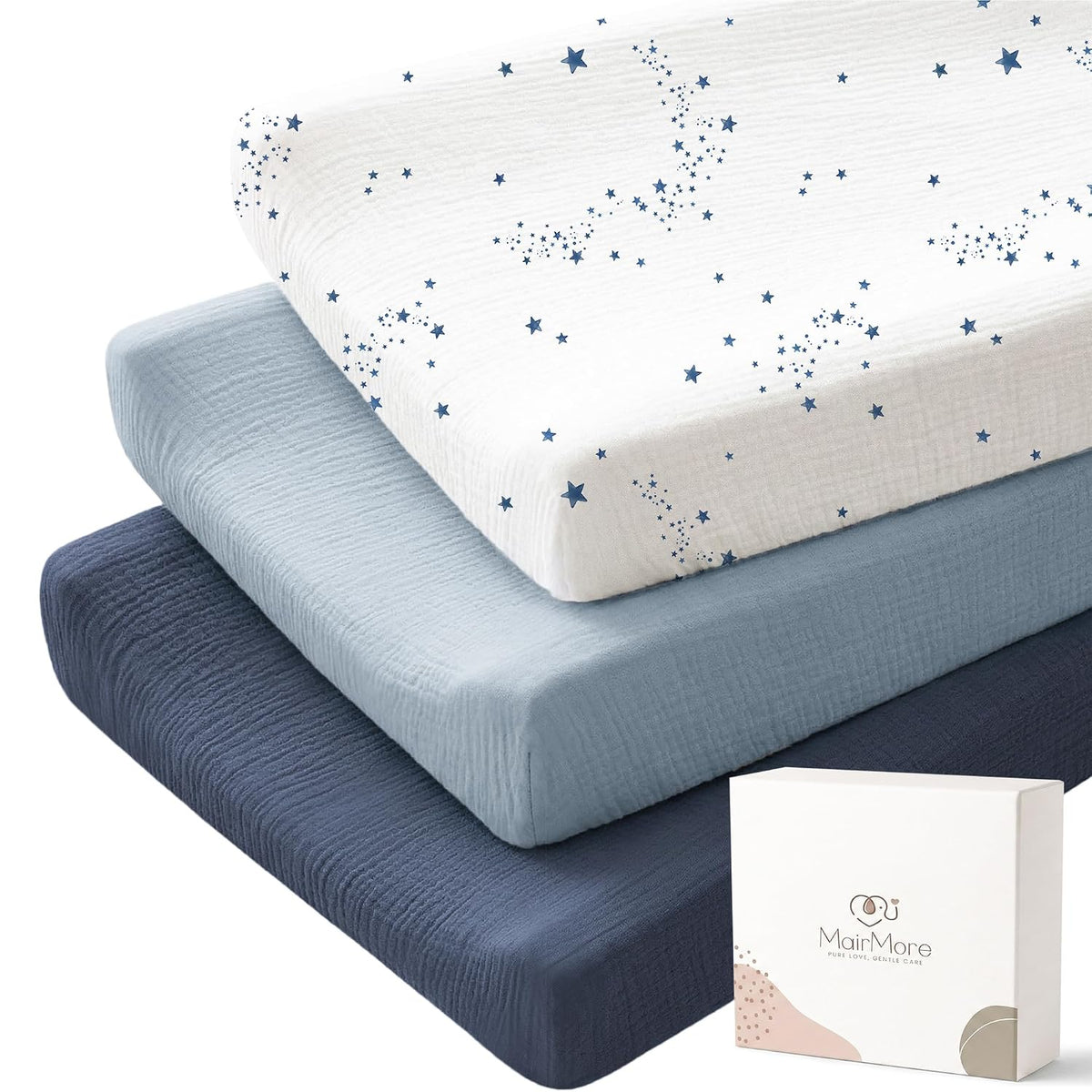 Three stacked changing pad covers in muslin fabric: top cover is white with navy star pattern, middle is solid light blue, bottom is solid dark navy. A white gift box with MairMore logo sits at lower right.