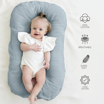Baby lying on a gray-blue muslin cotton lounger cover with textured fabric. Four icons on the right highlight product features: 100% Cotton, Breathable, Super Soft, and Long Lasting.