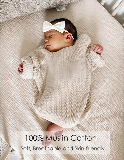 Sleeping newborn in a cream knit romper and white bow headband lying on a light beige muslin fitted crib sheet. Text overlay reads '100% Muslin Cotton - Soft, Breathable and Skin-friendly.'