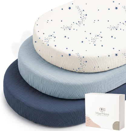 Three stacked oval bassinet fitted sheets by MairMore: top sheet is white with blue star constellation print, middle is solid light blue, bottom is solid navy. Textured muslin fabric visible. Product box shown at lower right.