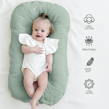 Baby lounger cover in sage green muslin cotton, shown with a smiling infant lying on it. Right side features four icons with labels: 100% Cotton, Breathable, Super Soft, and Long Lasting.
