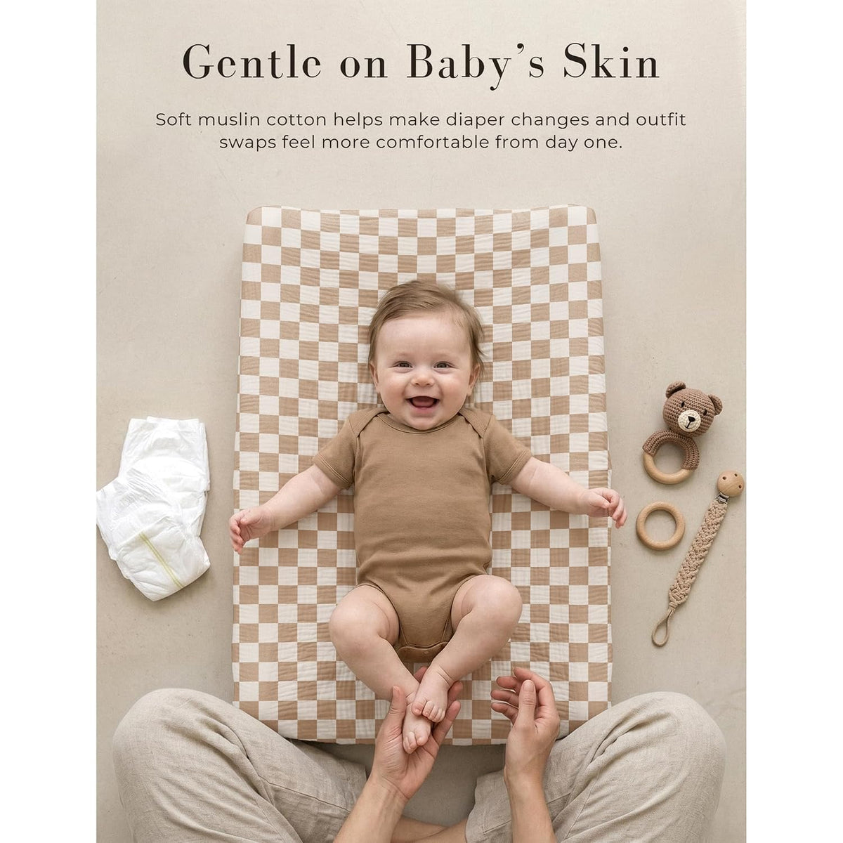 Baby lying on a changing pad covered with a tan and cream checkerboard muslin cotton cover. Text reads 'Gentle on Baby's Skin' with a note about soft muslin cotton for diaper changes.