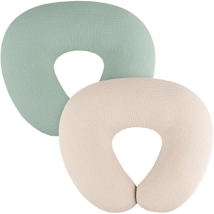Two U-shaped nursing pillow covers in a textured muslin fabric, shown overlapping. One is sage green, the other is light beige. Both feature a visible woven texture and a U-shaped opening at the bottom.