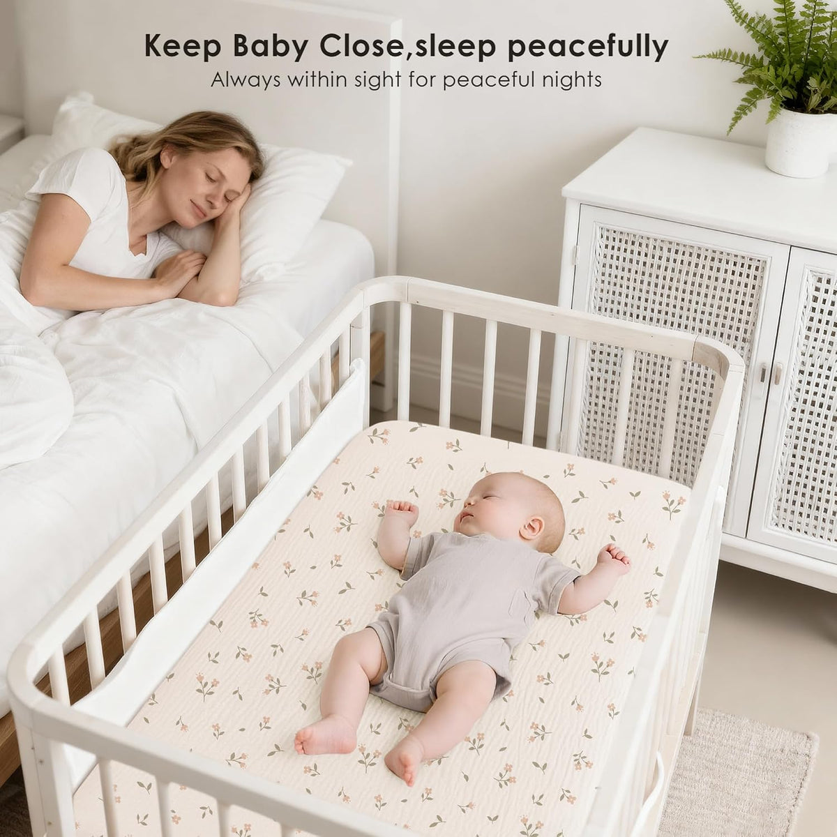 Lifestyle image of a white bedside bassinet with a sleeping baby on a cream fitted sheet featuring a small pink floral print. A woman sleeps peacefully in the adjacent bed. Text reads 'Keep Baby Close, sleep peacefully.'