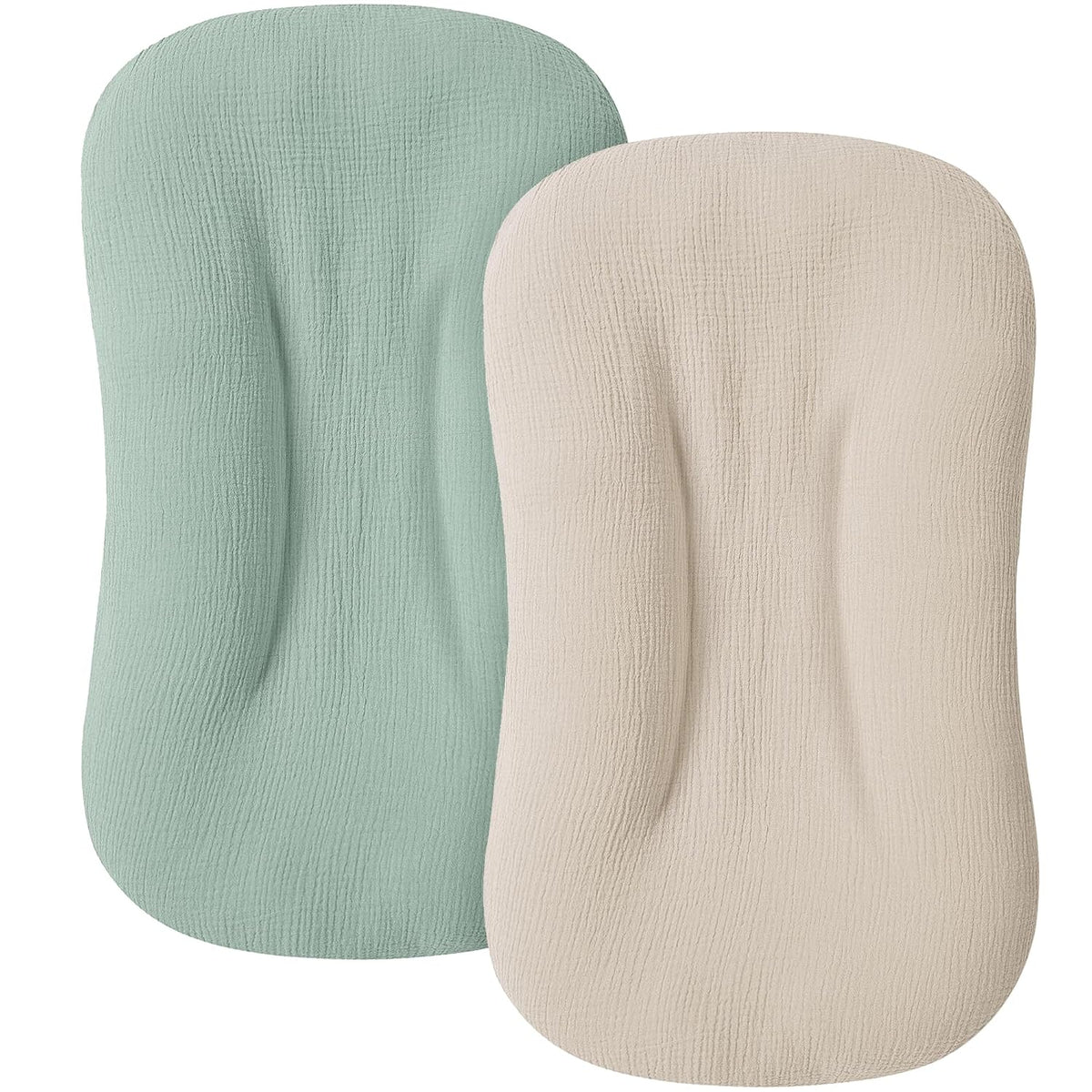 Two oval-shaped baby lounger slipcovers with textured muslin fabric, one in sage green and one in ivory/cream, shown overlapping on a white background. Both feature a contoured center indent.