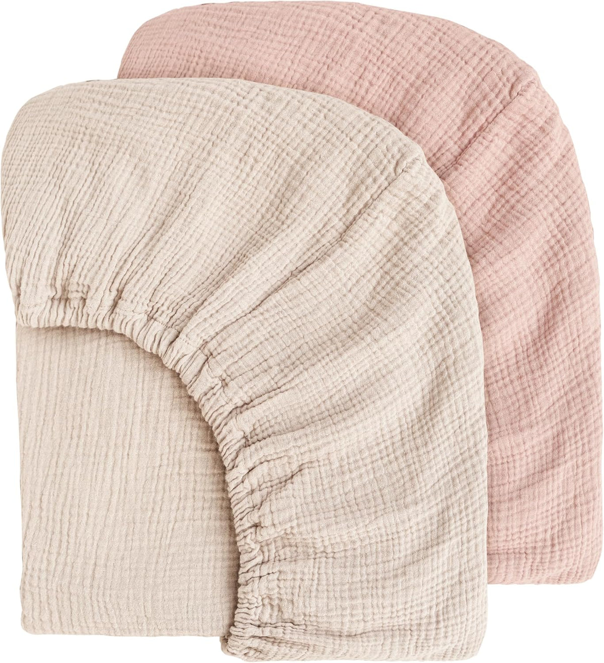 Two muslin fitted crib sheets displayed overlapping: a cream/ivory sheet in front and a dusty pink sheet behind. Both show visible gauze texture and elasticated edges with gathered corners, on a white background.
